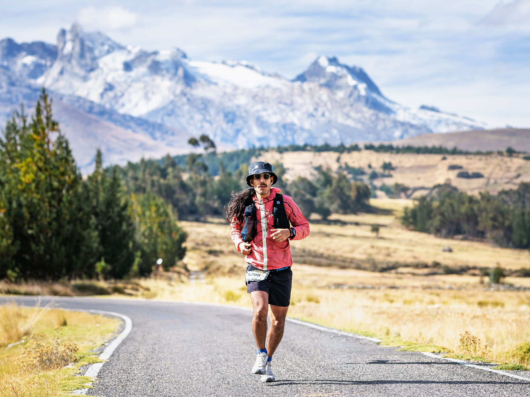 Giuseppe trail running on a mountain road with snow-capped Andean peaks in the background
